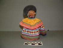 DOLL DRESSED IN SEMINOLE PATCHWORK DESIGNS AND IS ADORNED WITH BEADS